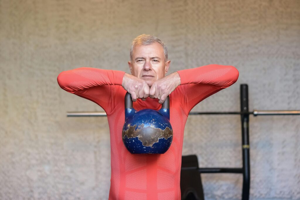 senior man in a red shirt lifting a kettlebell to his chin
