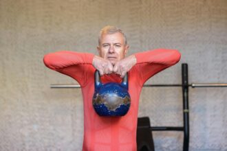 senior man in a red shirt lifting a kettlebell to his chin
