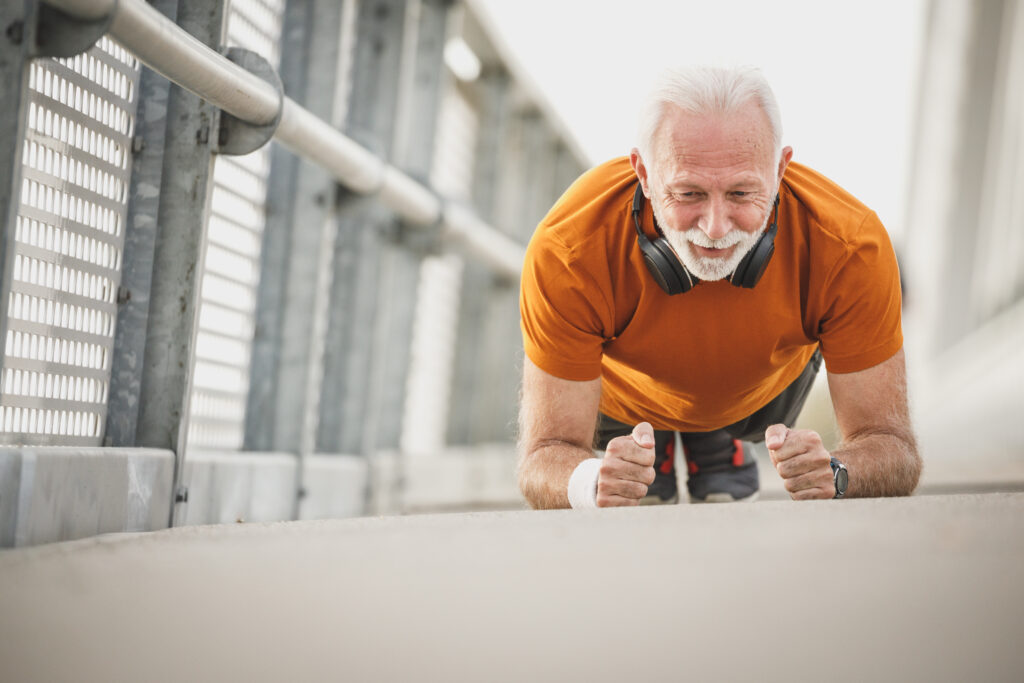 lean, fit, senior man in an orange shirt doing a plank and facing the camera